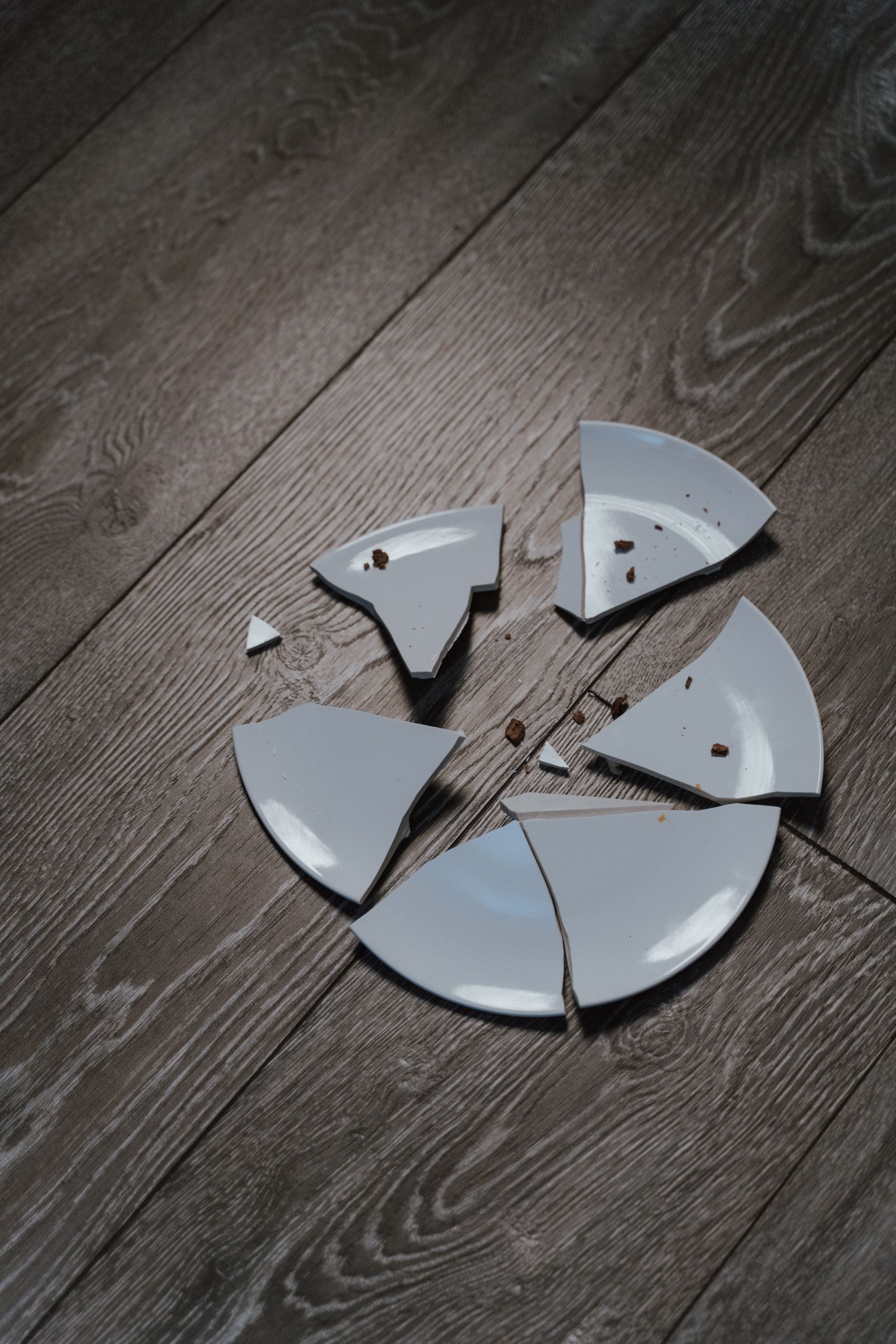 A broken white plate on a wooden floor